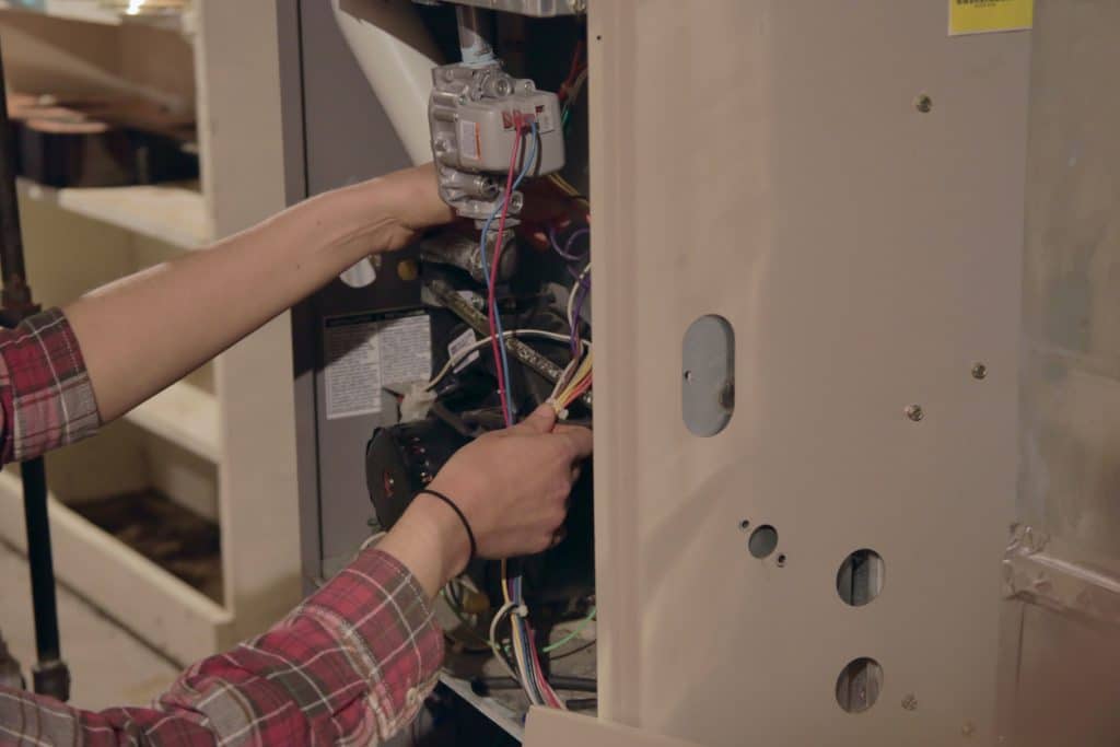 HVAC technician servicing the internal components and wiring of a residential furnace.