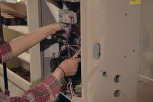 HVAC technician servicing the internal components and wiring of a residential furnace.