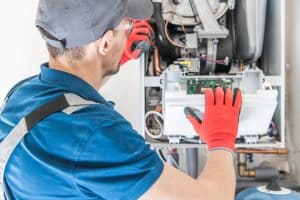 HVAC technician in protective gloves inspecting the internal electrical and control components of a furnace or heating system.